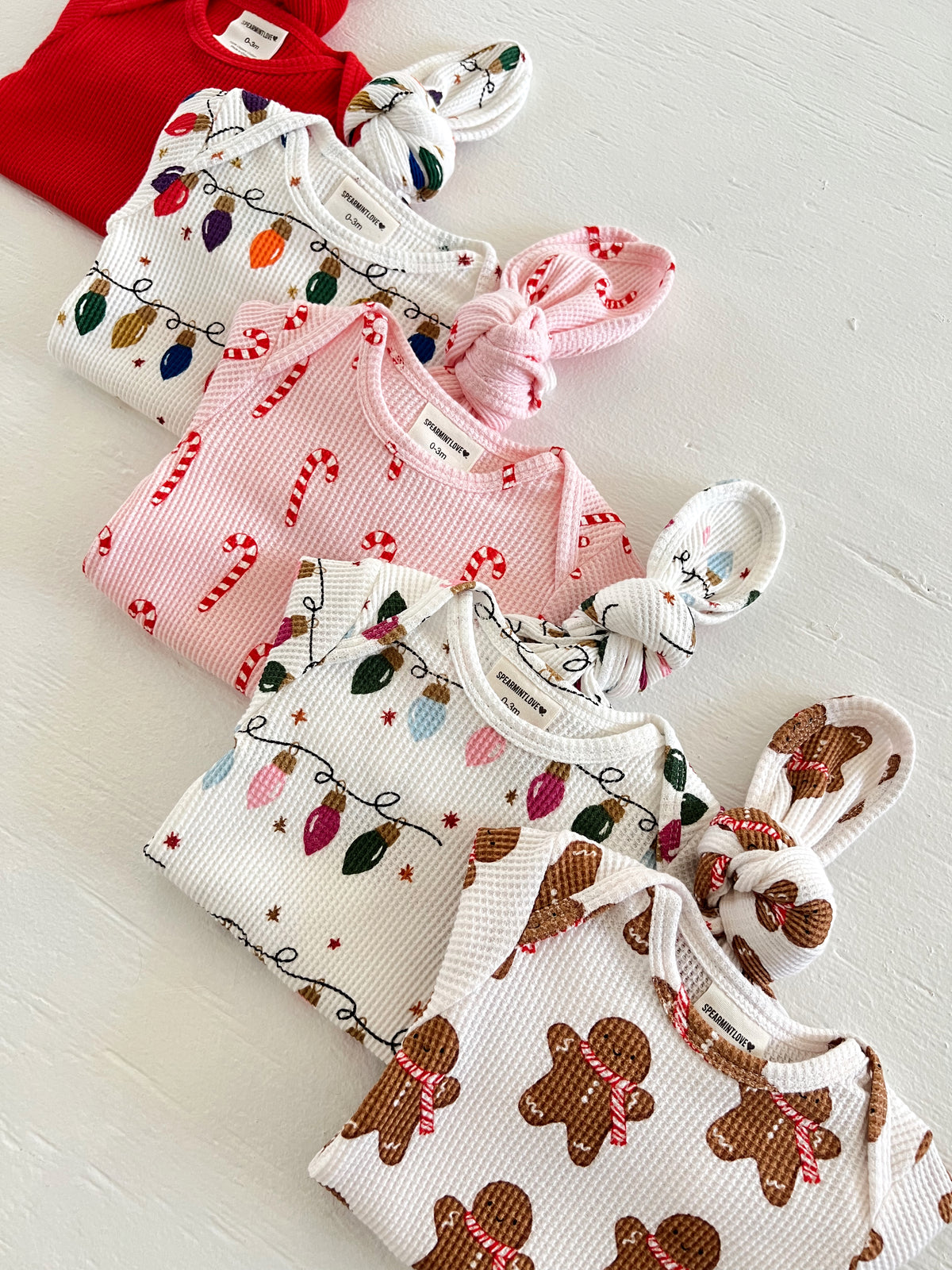 Four colorful baby outfits with festive designs: red, candy canes, holiday lights, and gingerbread patterns.