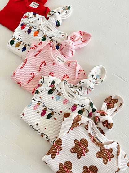 Four colorful baby outfits with festive designs: red, candy canes, holiday lights, and gingerbread patterns.