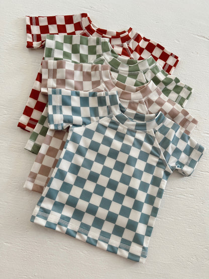 Colorful checkered short-sleeve shirts in red, green, blue, and beige stacked on a white surface.