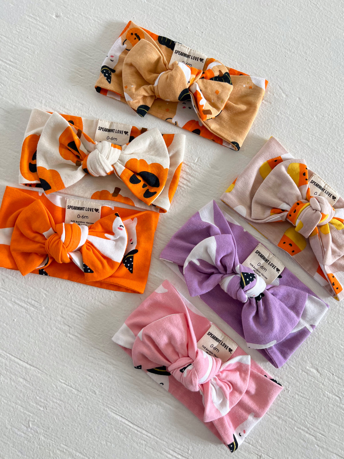 Six colorful baby headbands with bows, featuring various playful patterns and textures, displayed on a white surface.