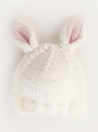 White knitted hat with pink inner bunny ears, resting on a white background.