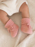 Baby's feet in cozy pink knitted booties on a soft cream blanket.