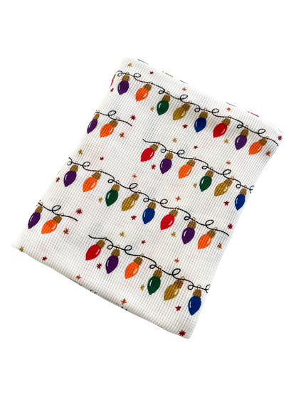 White fabric with colorful Christmas lights pattern and small stars, perfect for holiday decorations or gifts.
