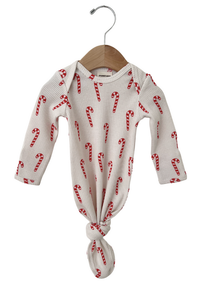 White baby onesie with red candy cane print, knotted at the bottom, hanging on a wooden hanger.