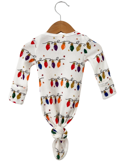 White outfit with colorful Christmas lights pattern, tied at the bottom, hanging on a wooden hanger.