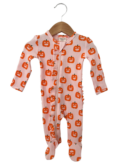 Infant onesie with orange pumpkin print on light pink background, hanging on a wooden hanger.