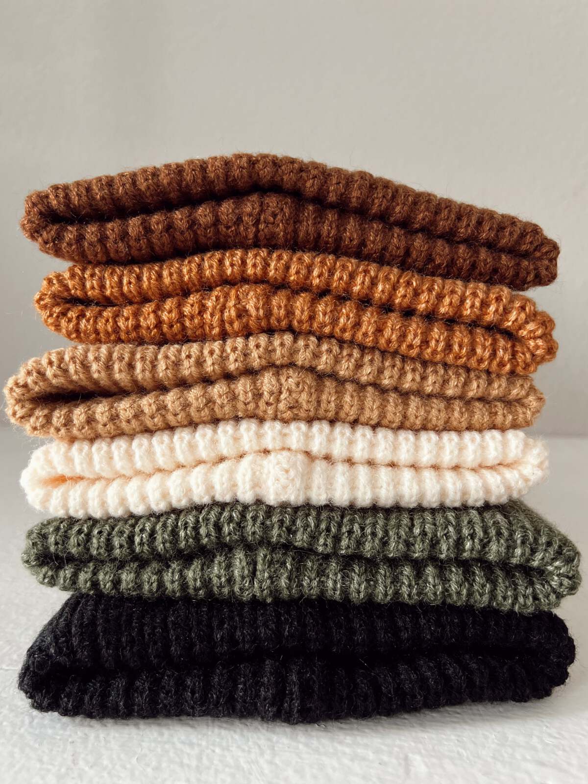 Stack of knitted fabric pieces in earthy tones: brown, orange, cream, green, and black, arranged neatly.