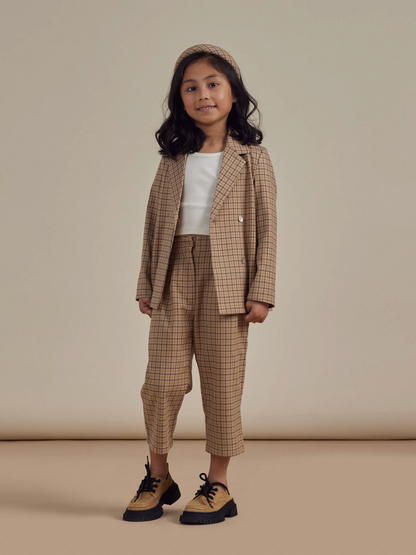 Girl in stylish plaid suit with a headband, standing against a neutral background, smiling confidently.