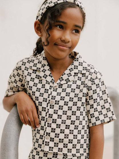 Young girl in patterned outfit, smiling and leaning on a railing, wearing a matching headband.