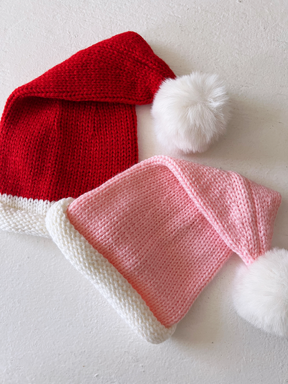 Two festive knitted hats: one red with a white brim and pom-pom, and one pink with a white brim and pom-pom.