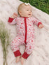 Smiling baby in floral-patterned onesie, lying on a soft blanket with greenery around.