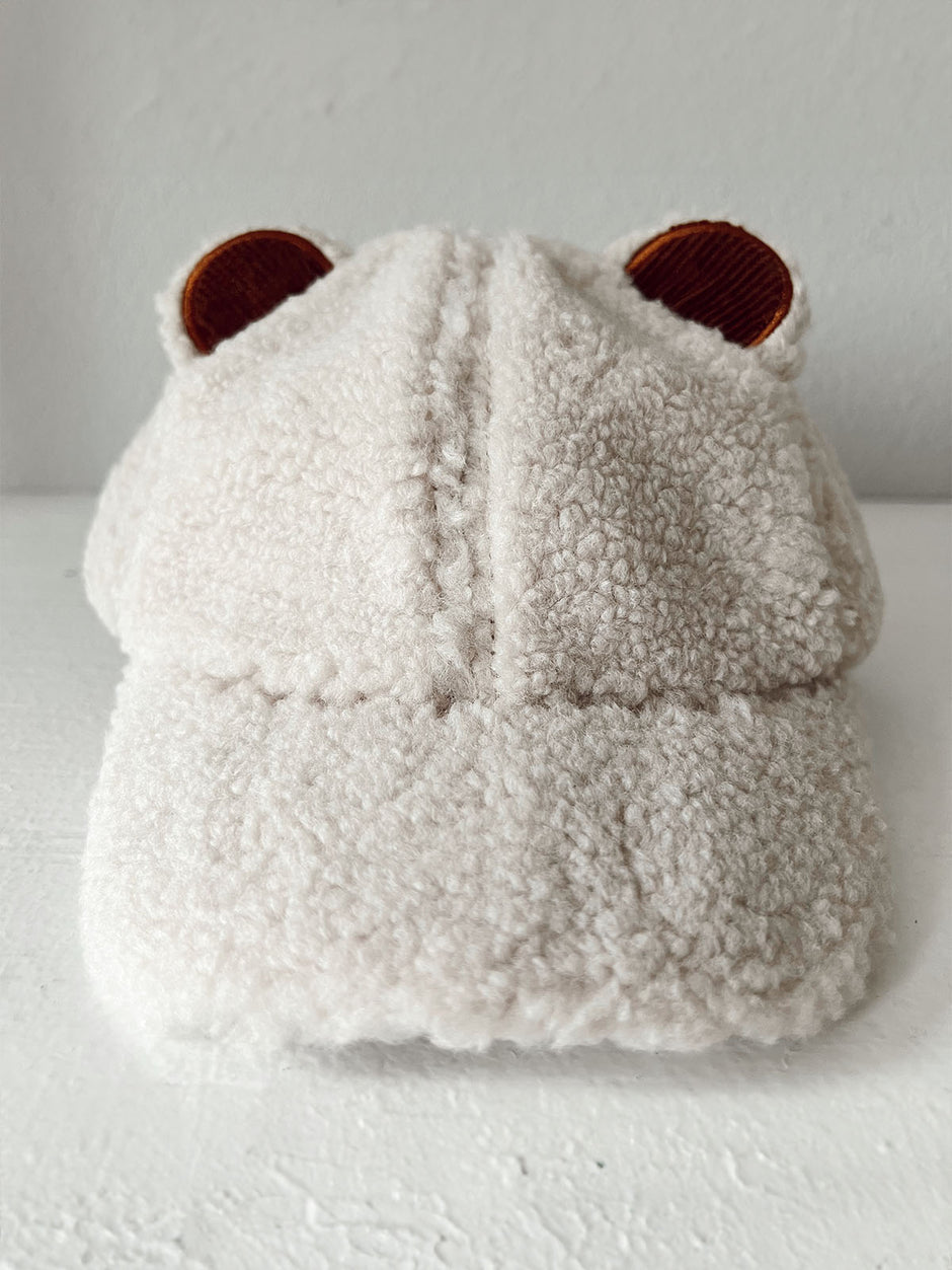 Fluffy beige cap with bear ears displayed on a white surface against a plain background.