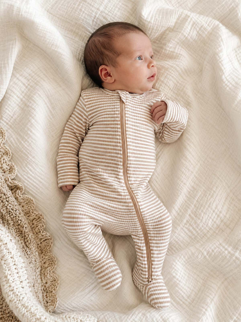 Baby in a striped sleeper lies on a soft blanket, looking up with a curious expression.