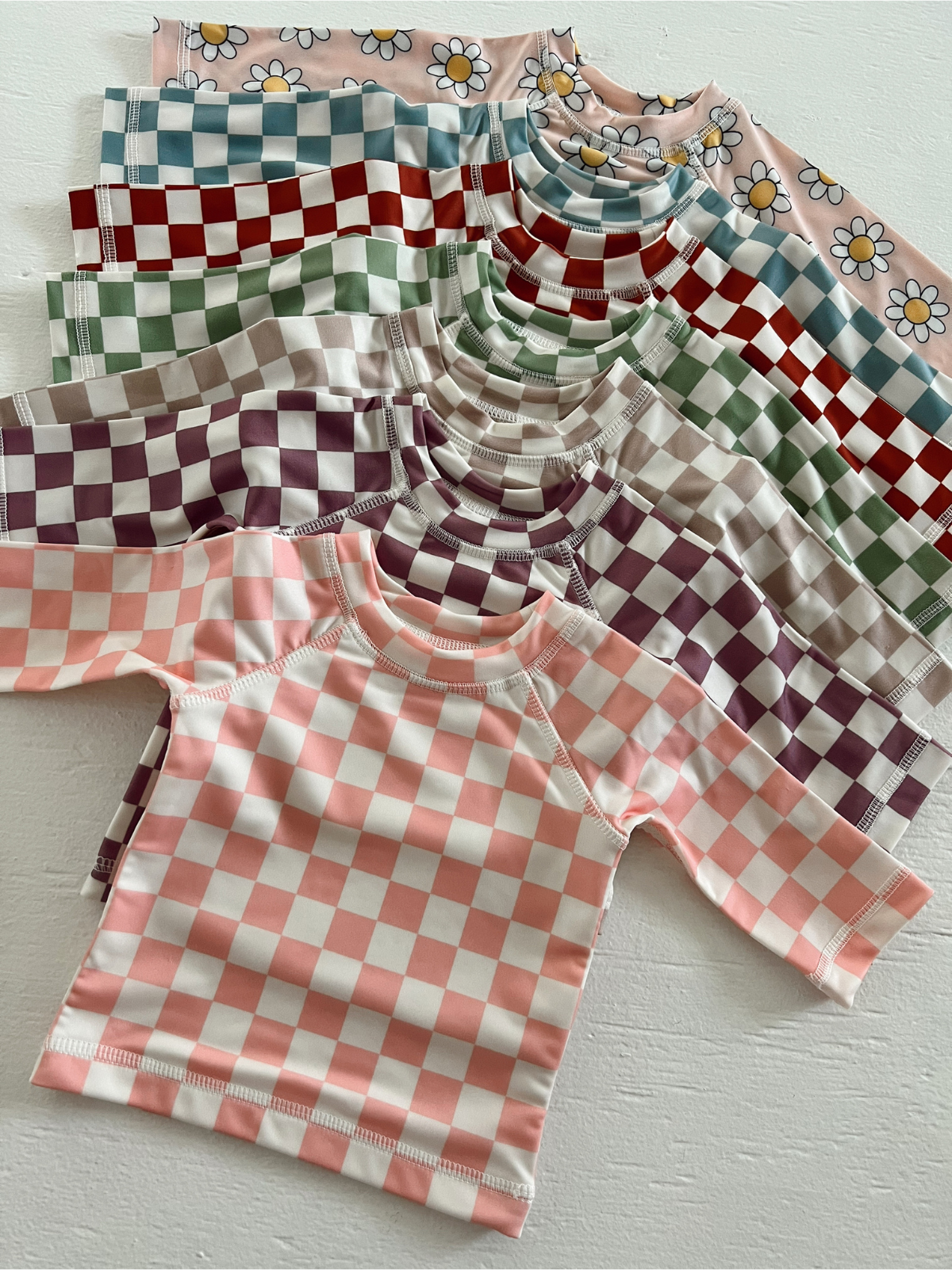 Colorful checkered and floral short-sleeve shirts arranged in a fan pattern on a light background.