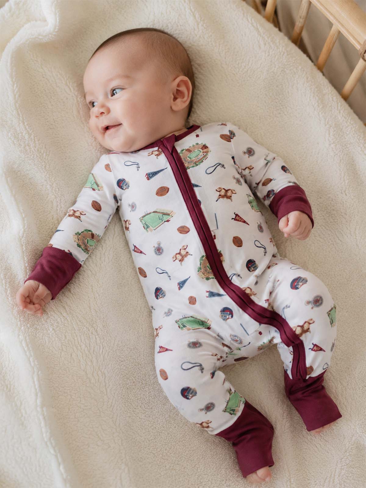 Smiling baby in patterned pajamas lying on a soft blanket, surrounded by a cozy nursery setting.