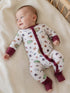 Smiling baby in patterned pajamas lying on a soft blanket, surrounded by a cozy nursery setting.