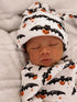 Sleeping baby wrapped in a bat and pumpkin-patterned blanket, wearing a matching hat.