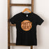Black t-shirt hanging on a wooden ladder, featuring "Pretty Neat" graphic design in vibrant colors.