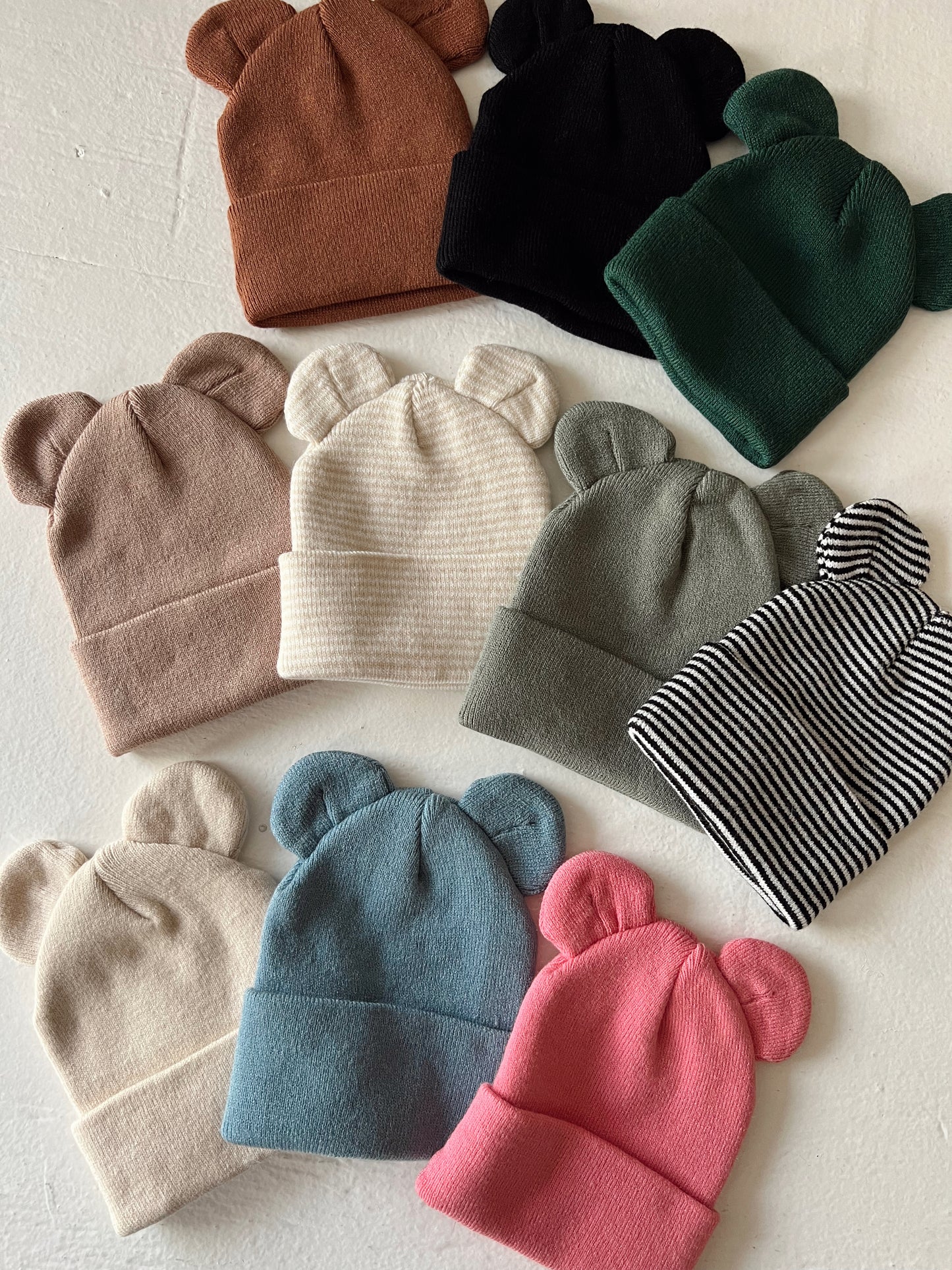 Colorful bear-ear beanies arranged on a light background, showcasing various styles and colors.