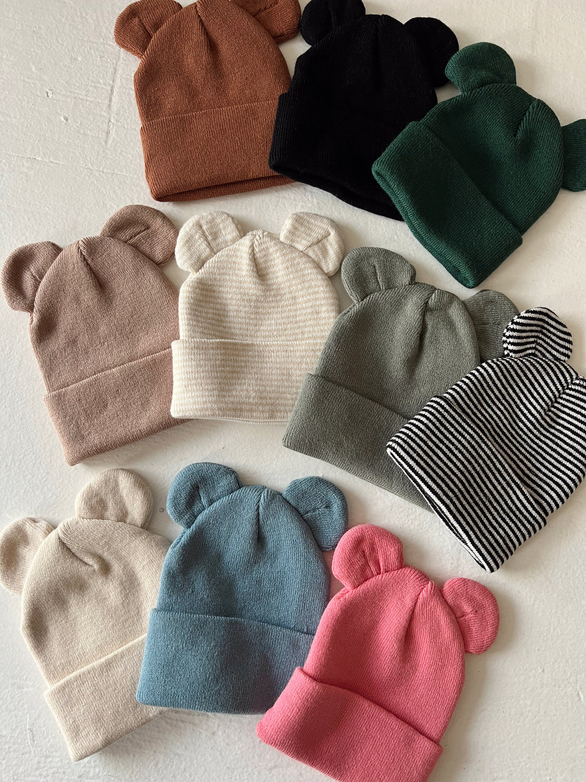 A collection of colorful bear-ear beanies arranged on a light background.
