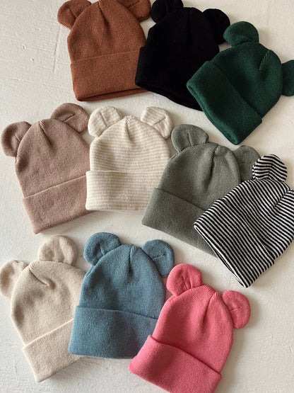 A collection of colorful bear-ear beanies arranged on a light background.