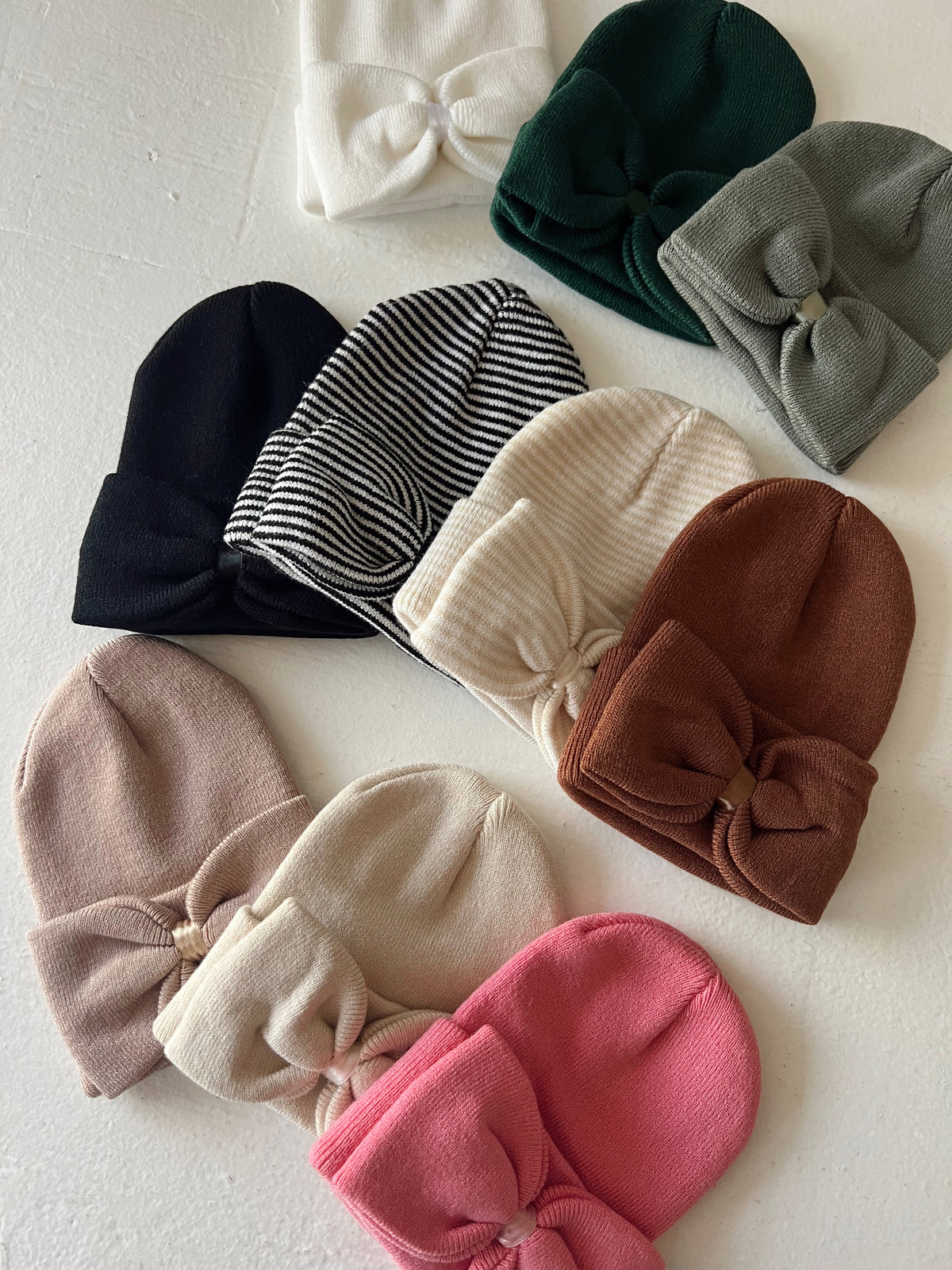 Assorted baby beanies in various colors and styles, featuring bows on some and a striped pattern.