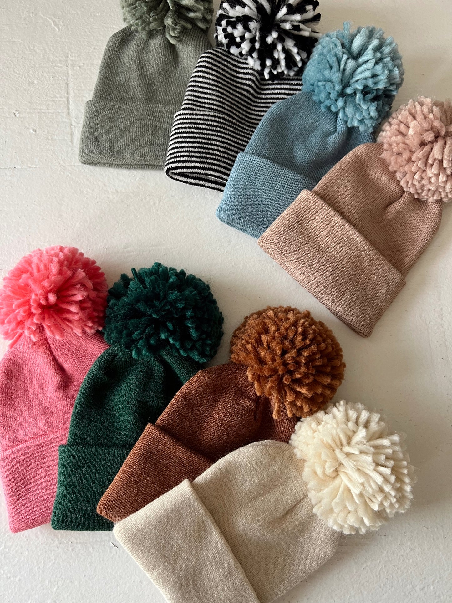 Colorful knitted beanies with pom-poms displayed on a light background, showcasing various styles and textures.