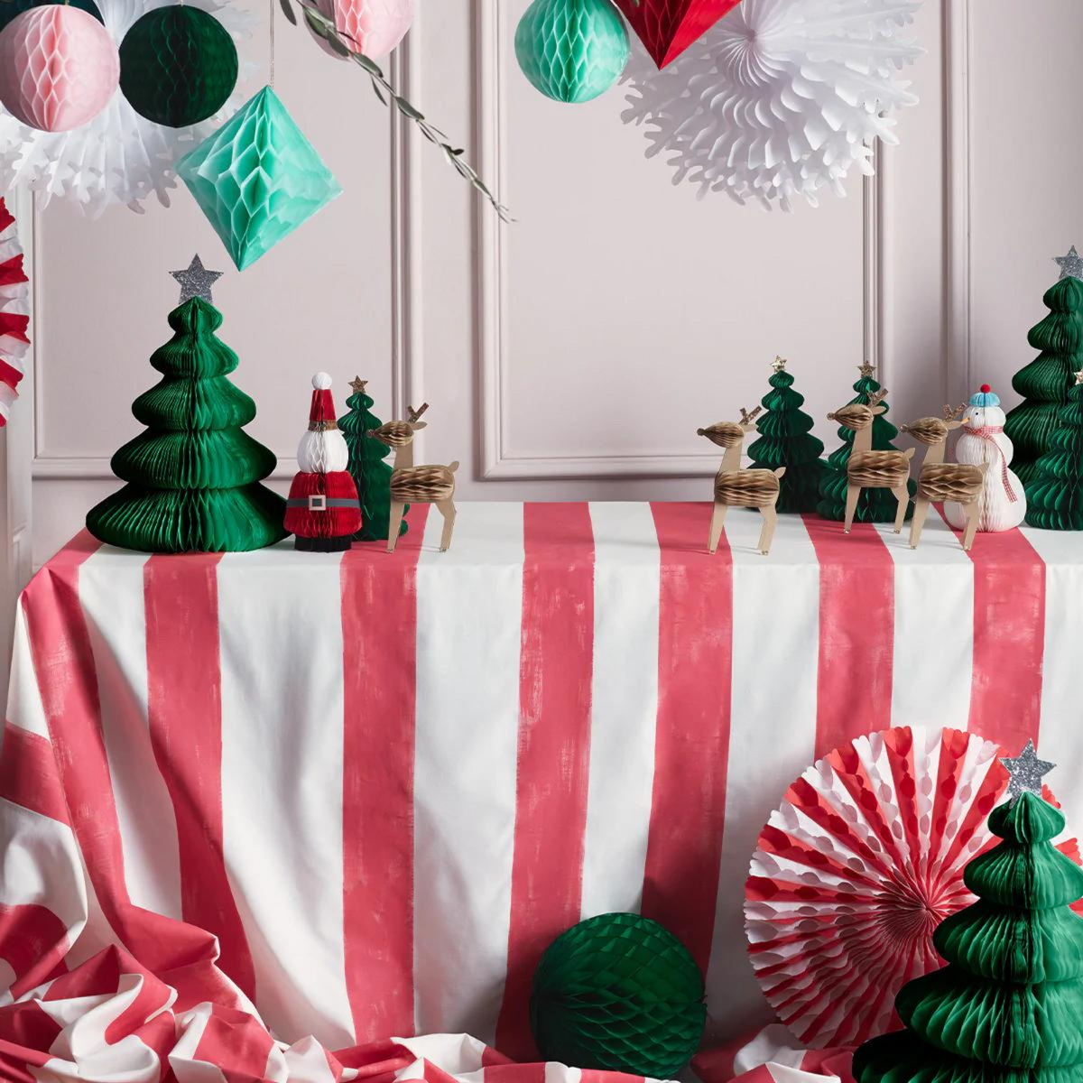 Festive table display with red and white striped cloth, green trees, wooden reindeer, and holiday decorations.