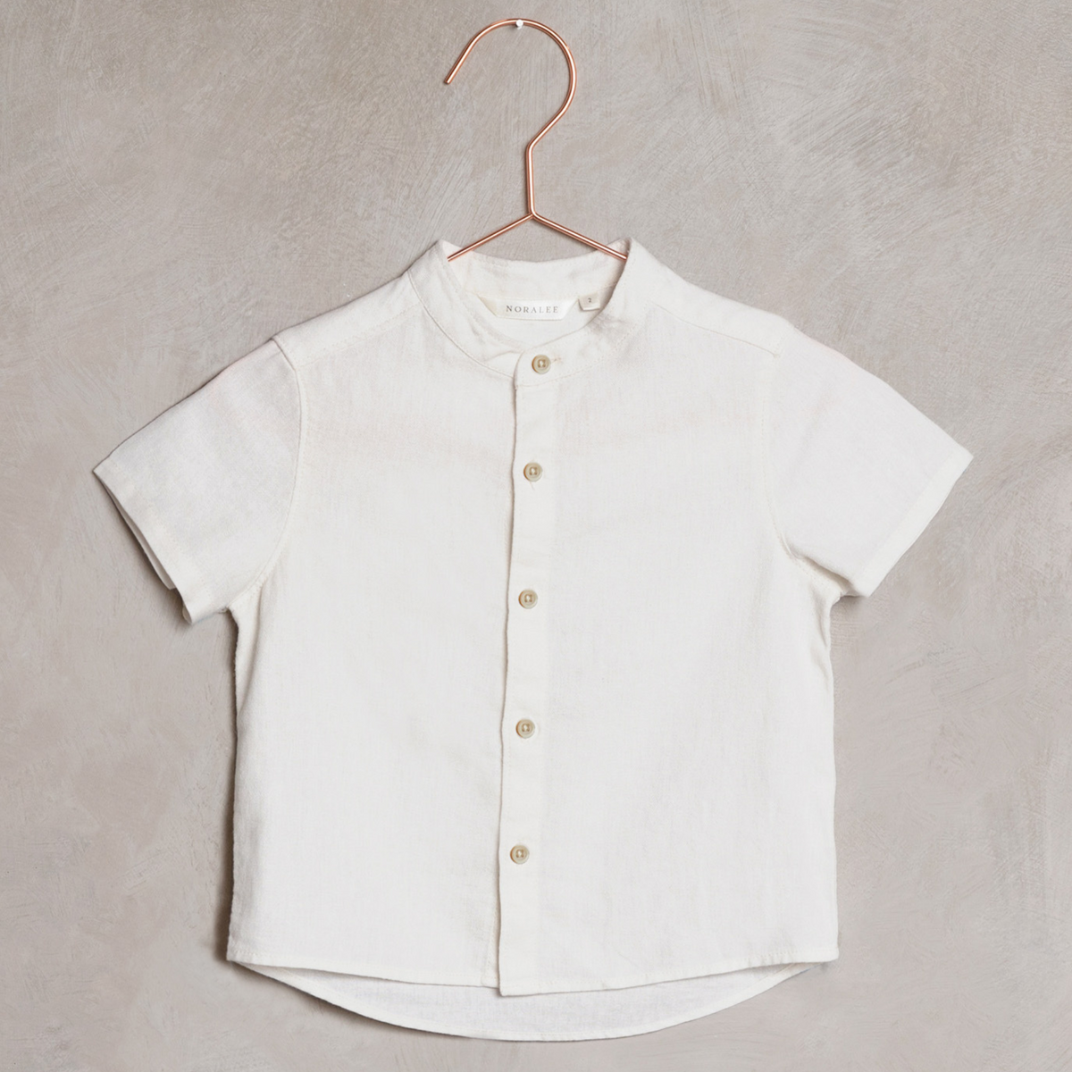 Short-sleeve white button-up shirt hanging on a copper hanger against a textured background.
