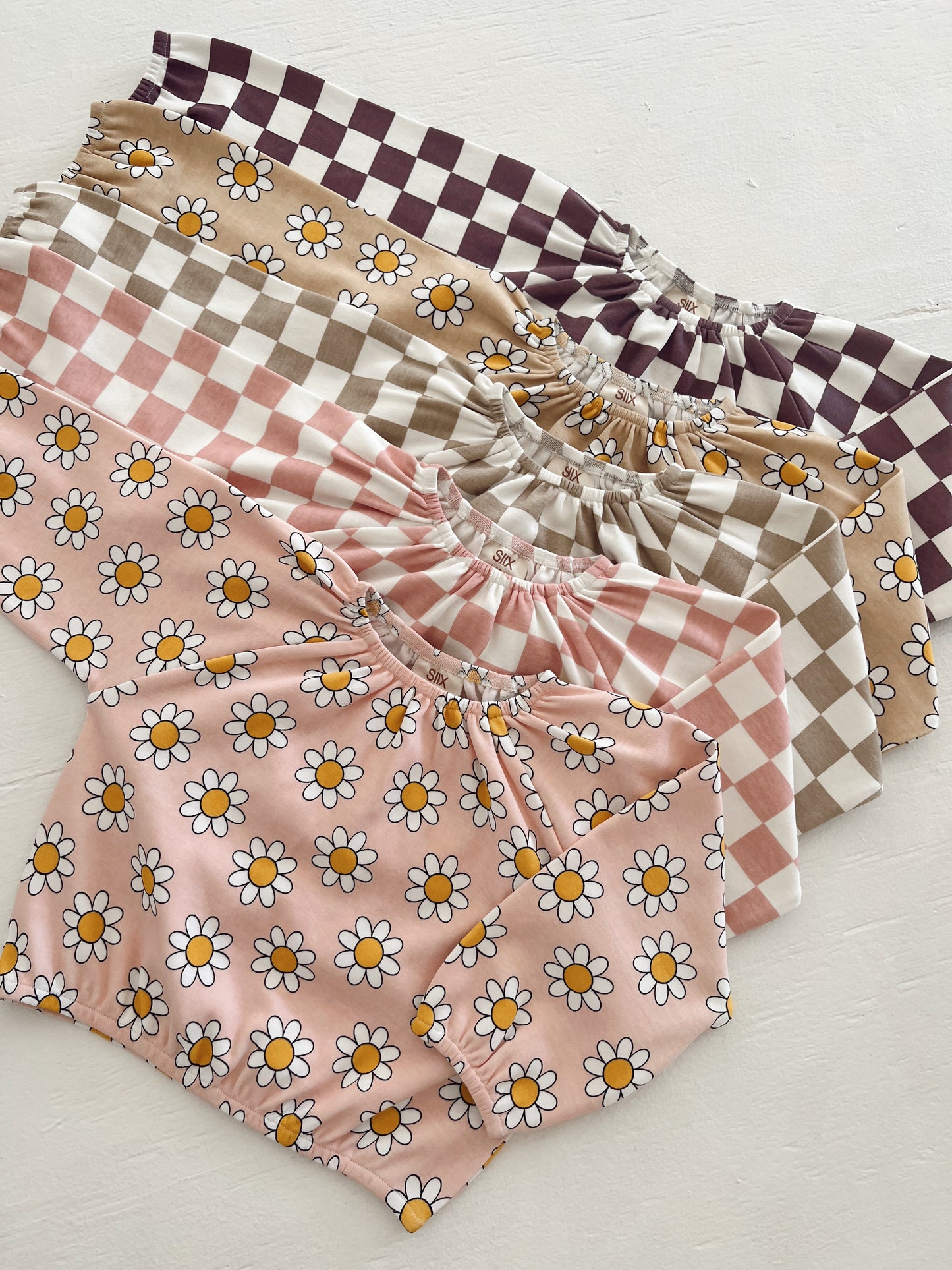 Assorted children's clothing featuring floral and checkered patterns in pastel colors.