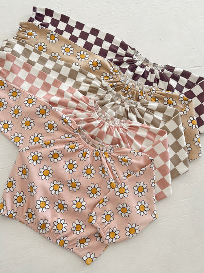 Assorted children's clothing featuring floral and checkered patterns in pastel colors.