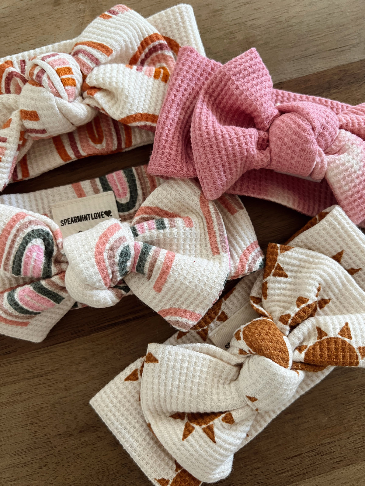 Four colorful fabric headbands with bows, featuring various patterns in pink, orange, and white.