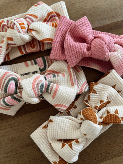 Four colorful fabric headbands with bows, featuring various patterns in pink, orange, and white.