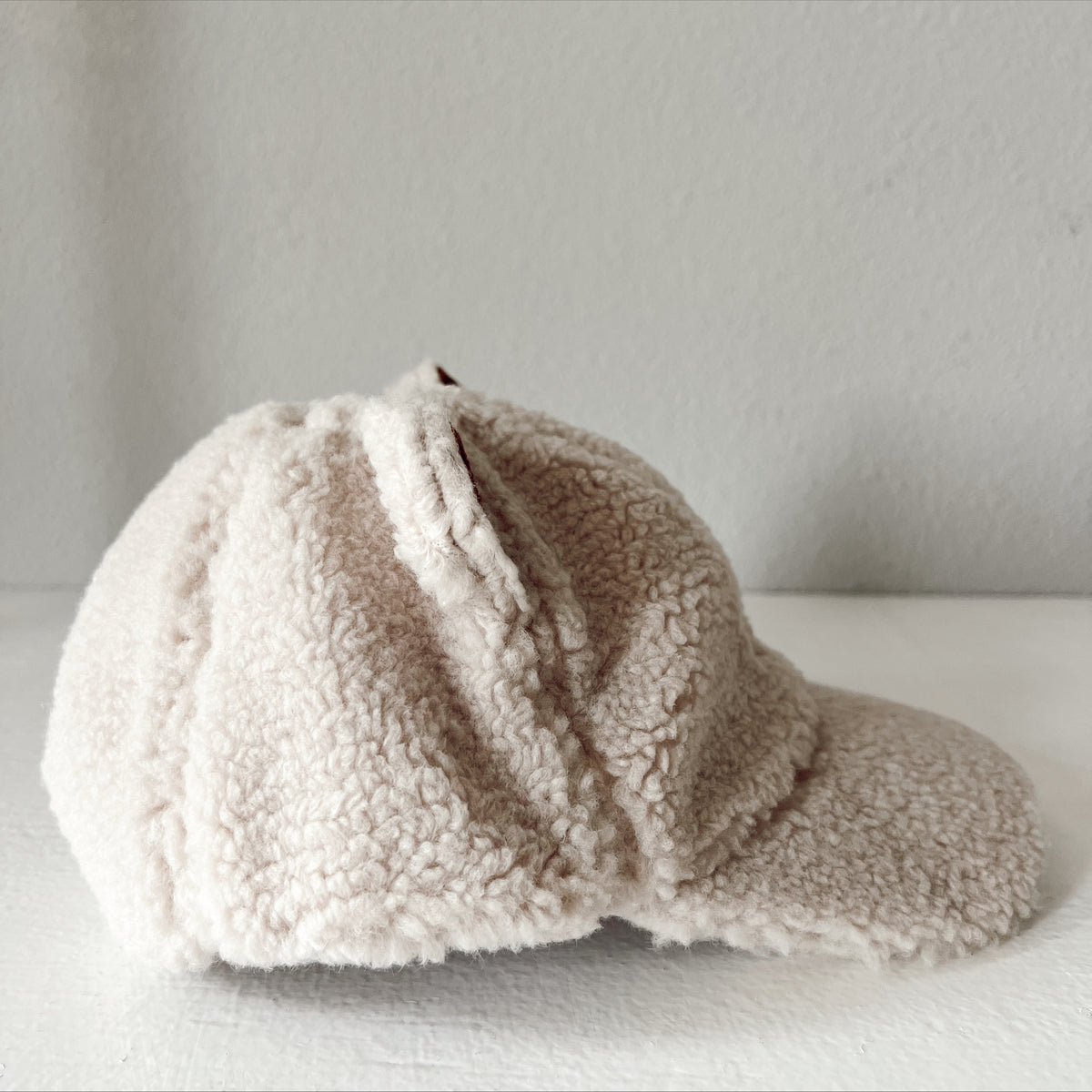 Side view of a soft beige furry cap resting on a white surface.