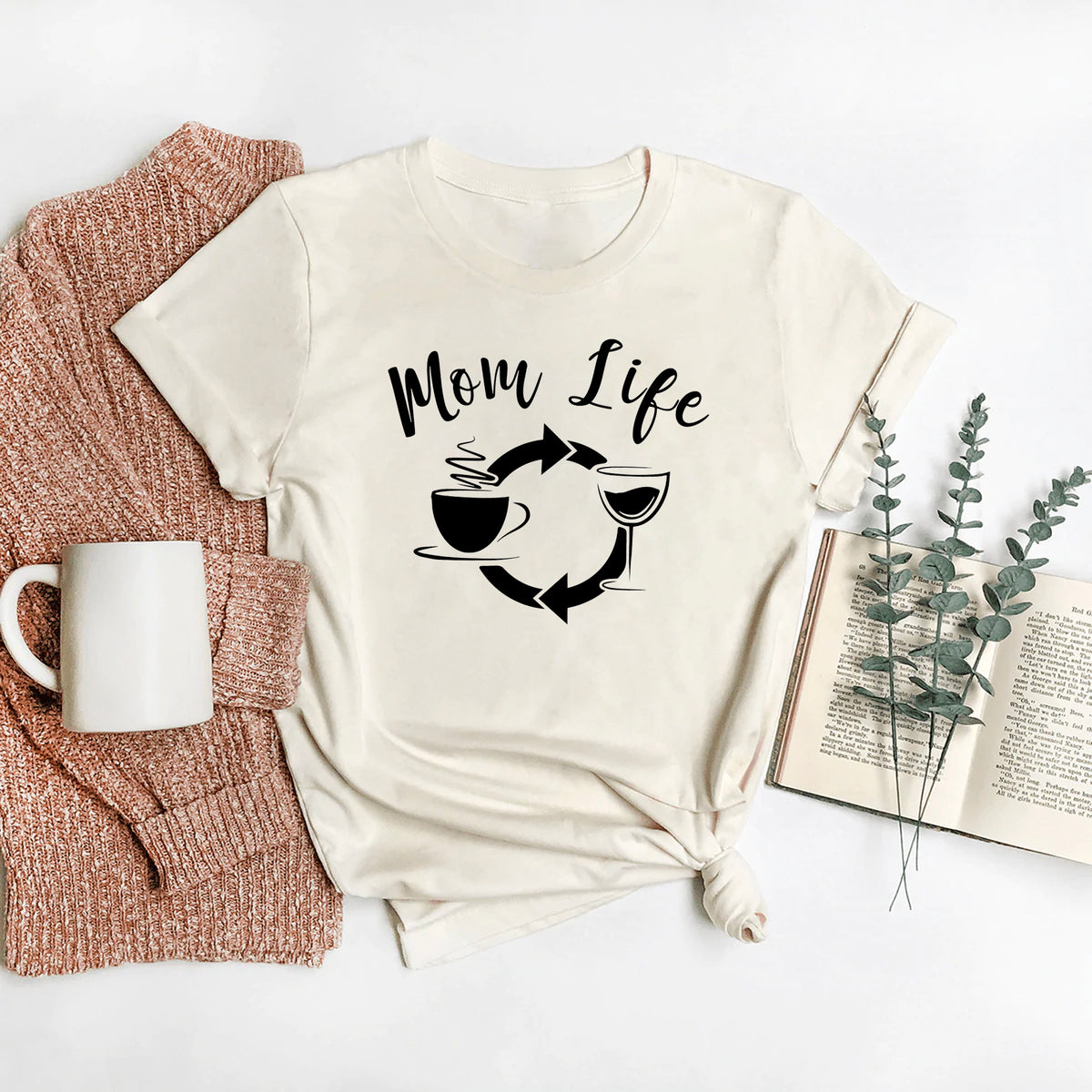 Cream t-shirt with "Mom Life" graphic, coffee cup and wine glass icons, styled with knit cardigan, mug, and book.